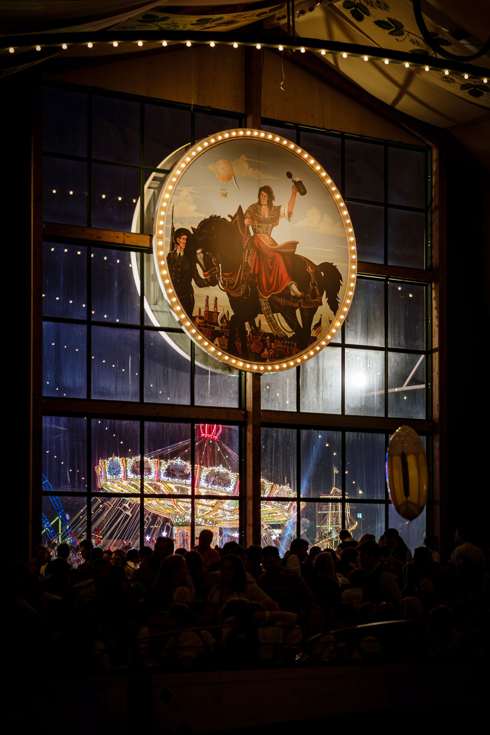 Blick aus dem Bräurosl-Festzelt auf die beleuchteten Fahrgeschäfte des Oktoberfests bei Nacht